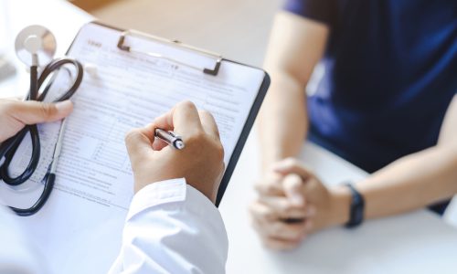 Close-up of a male doctor hand hold a silver pen and showing pad in hospital. Doctor giving prescription to the patient and filling up medical form at a clipboard