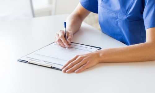 medicine, people and healthcare concept - close up of female doctor or nurse writing medical report to clipboard at hospital